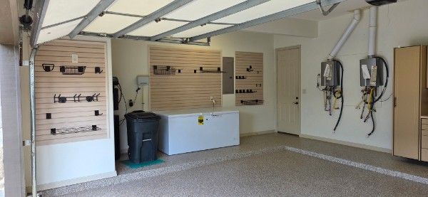 Empty garage with slatwall storage, shelves, a trash bin, and wall-mounted hoses on the right.