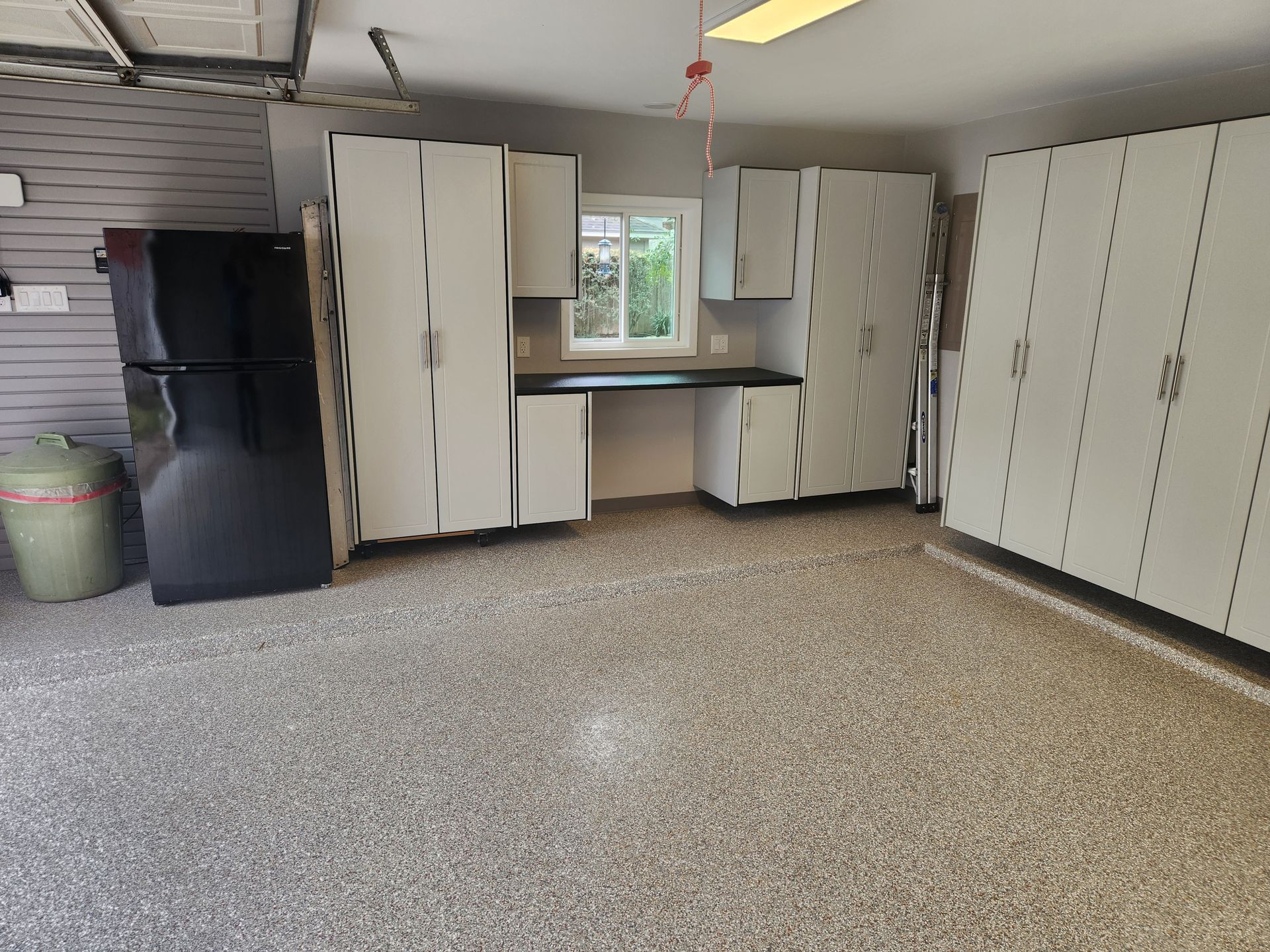Garage with white storage cabinets, a black refrigerator, and a speckled floor.