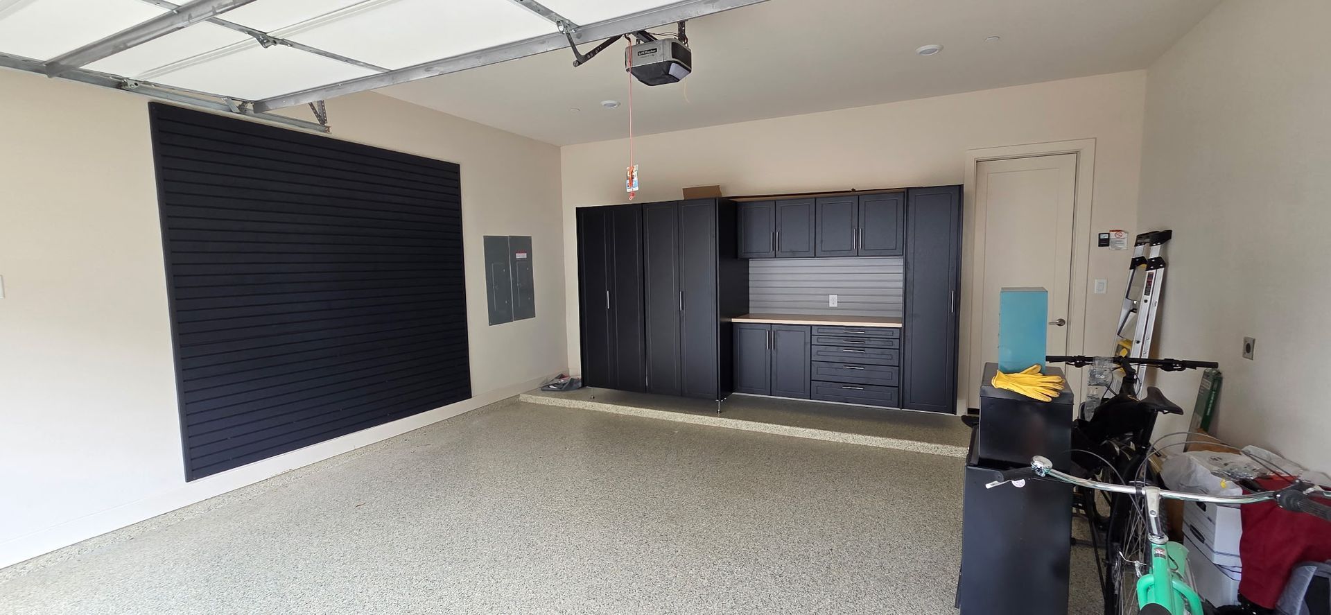 Empty room with a large black wall panel, gray carpet, and dark cabinets along the back wall.