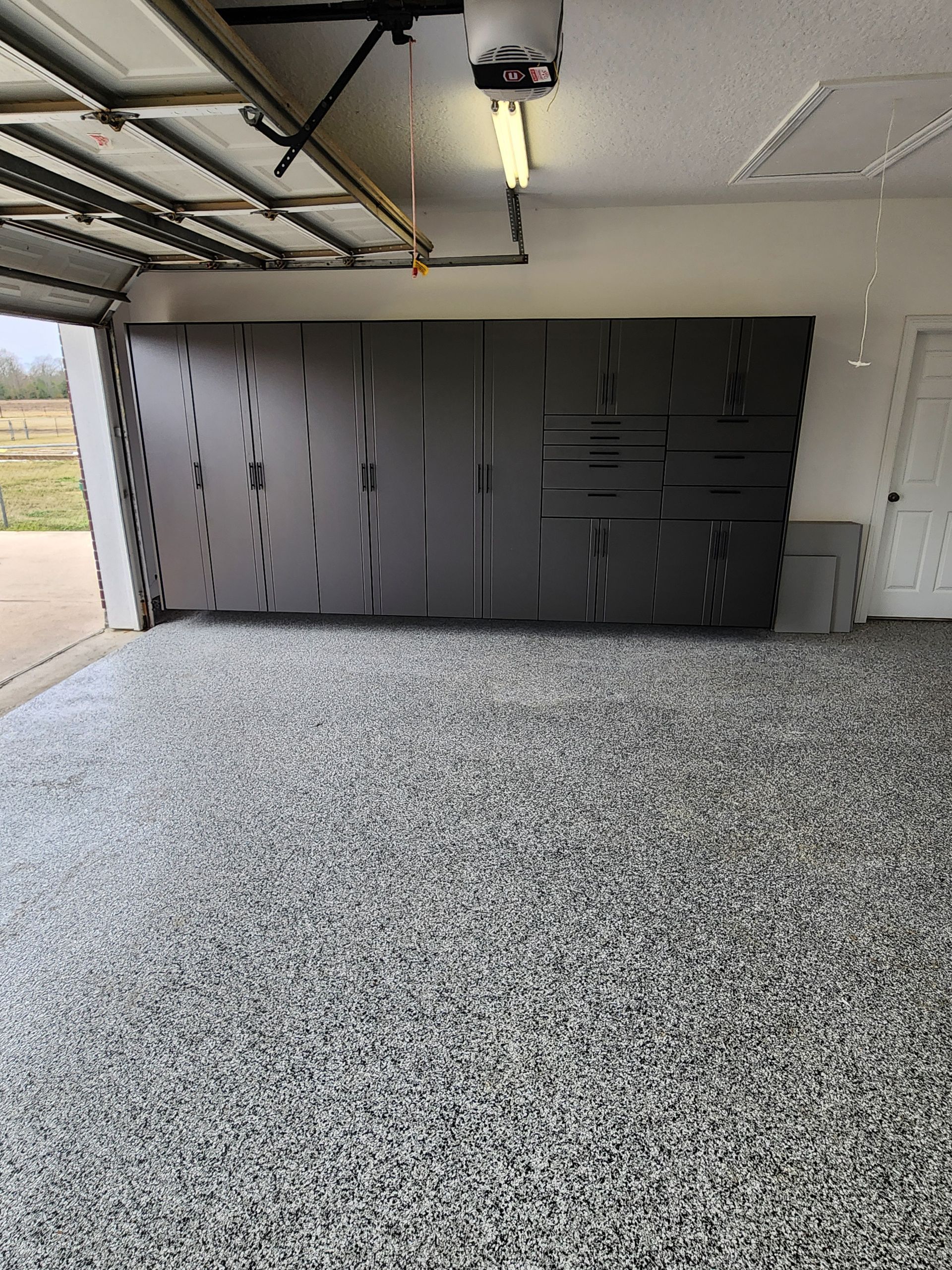 Gray epoxy-floored garage with a large black storage wall under the open ceiling.