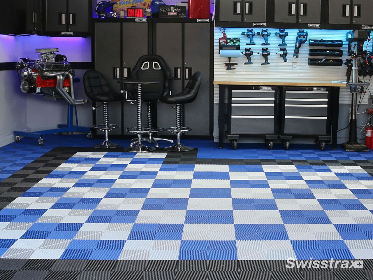 Blue-and-white checkered garage floor with cabinets, workbench, and two black chairs along the back wall