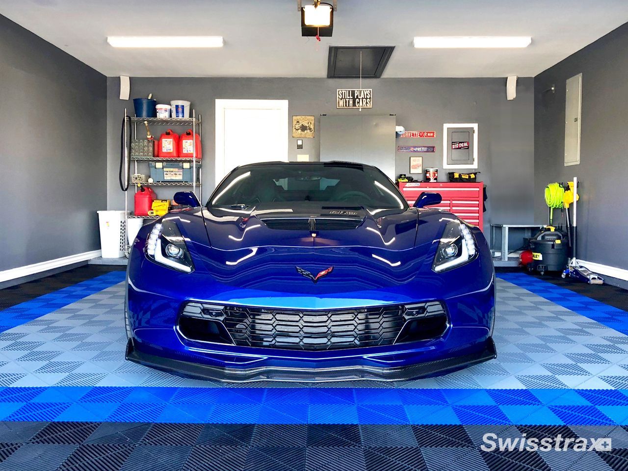 Blue sports car parked in a garage with blue checkered floor and tool cabinets behind it