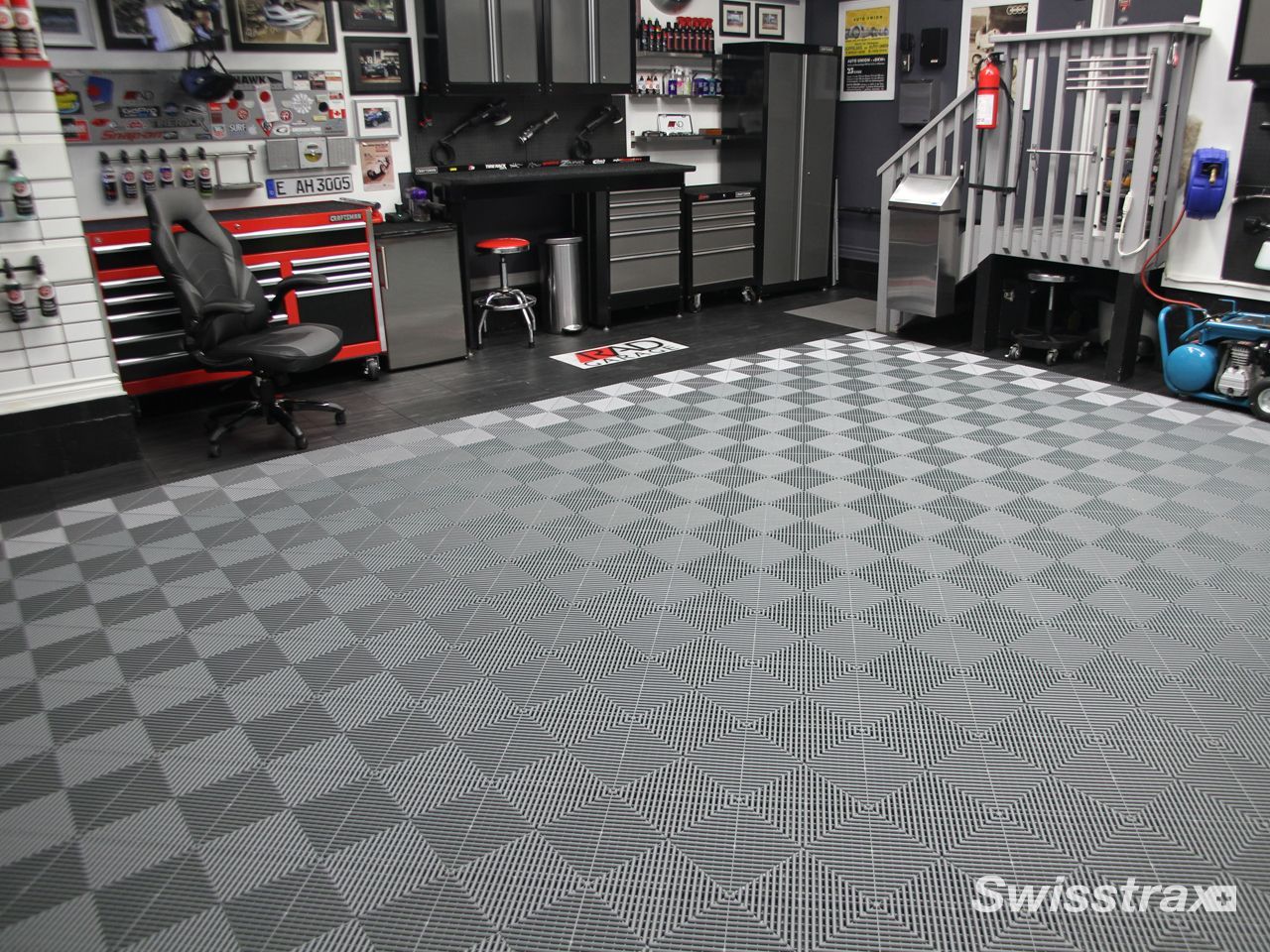 Garage workshop with gray patterned floor mats, tool cabinets, and wall-mounted tools.