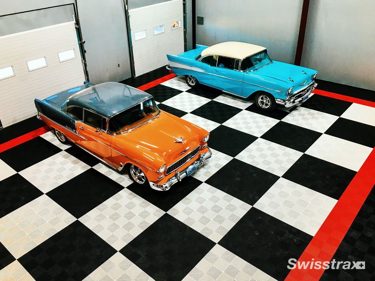 Two classic cars, orange and turquoise, parked on a black-and-white checkered floor in a showroom.