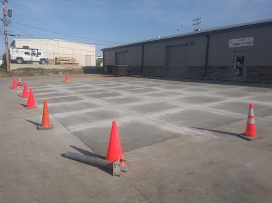 A row of orange traffic cones are lined up in a parking lot in front of a building.
