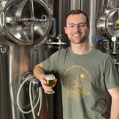 a man stands next to tanks with a glass of beer