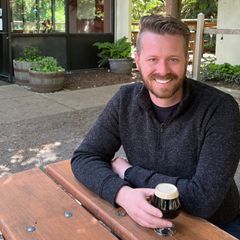 a man with a beard is smiling and holding a glass of beer