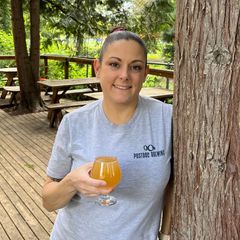 a woman leans on a tree with a glass of beer