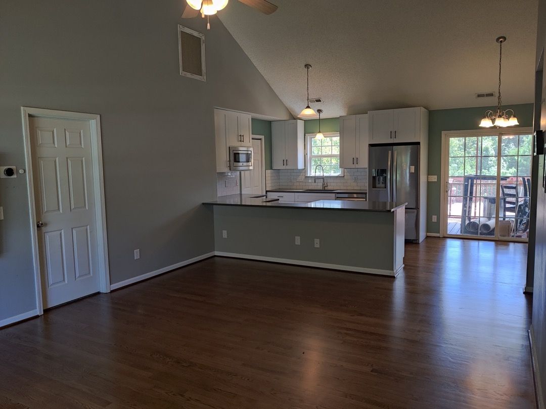 An empty living room with hardwood floors and a kitchen.