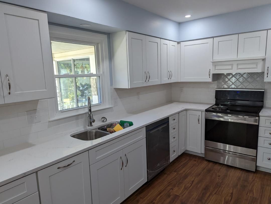 A kitchen with white cabinets , stainless steel appliances , a sink , and a window.