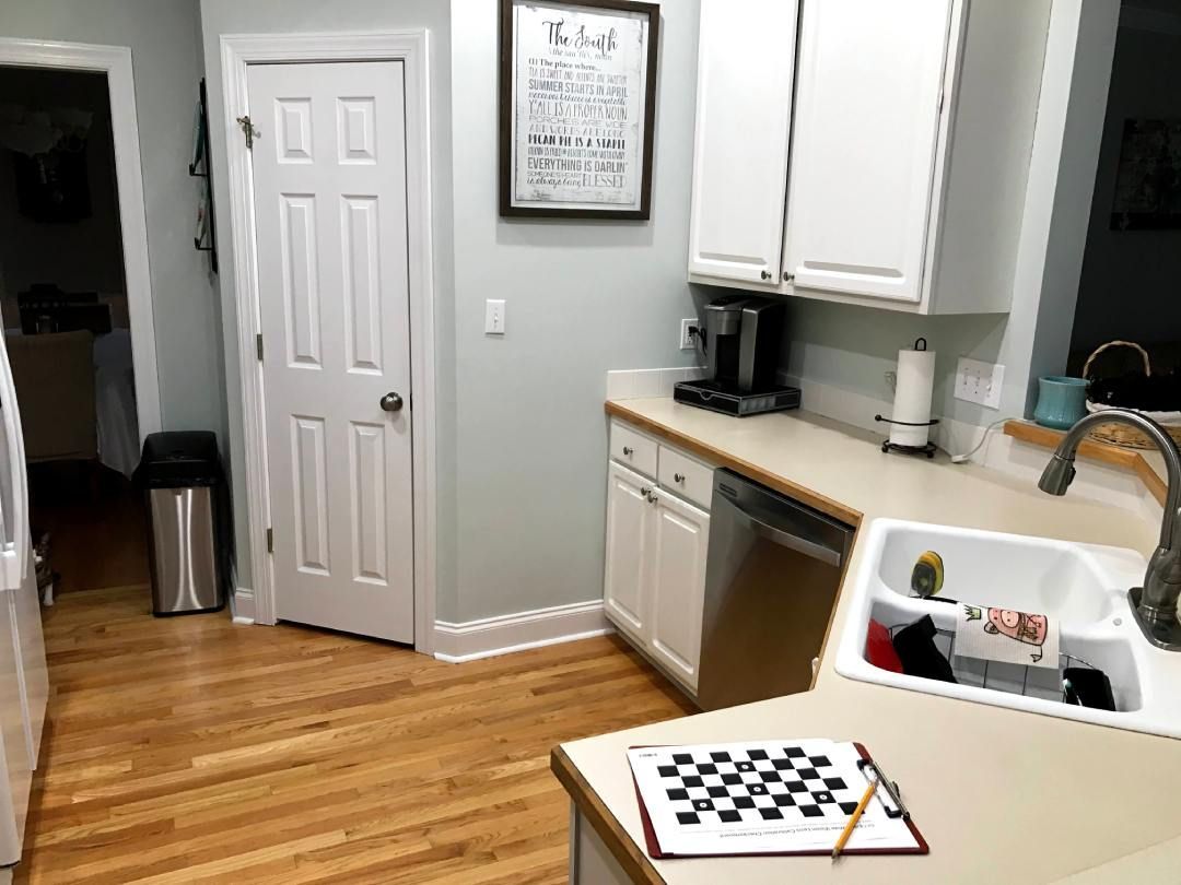 A kitchen with white cabinets , a sink , and a chess board on the counter.