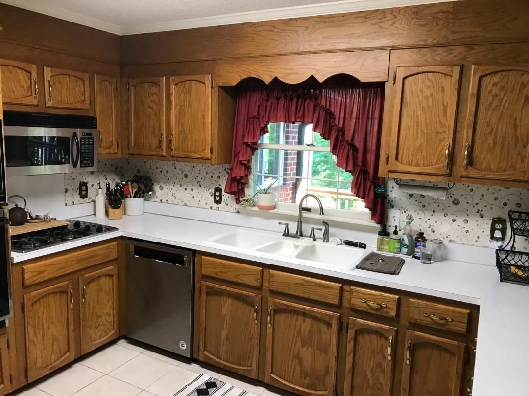 A kitchen with wooden cabinets , stainless steel appliances , a sink , and a window.