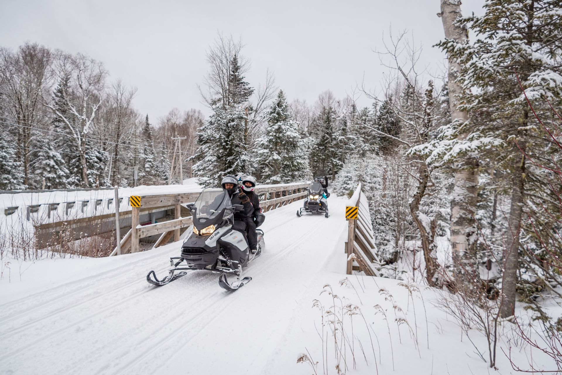 a couple riding a snowmobile on a snowy bridge