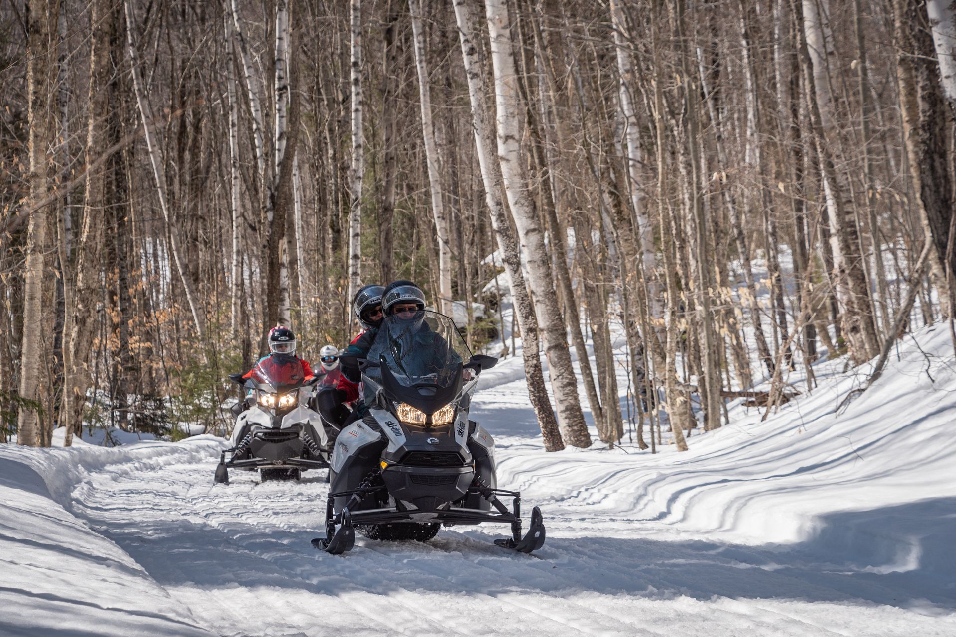 a group of people are riding snowmobiles down a snowy path