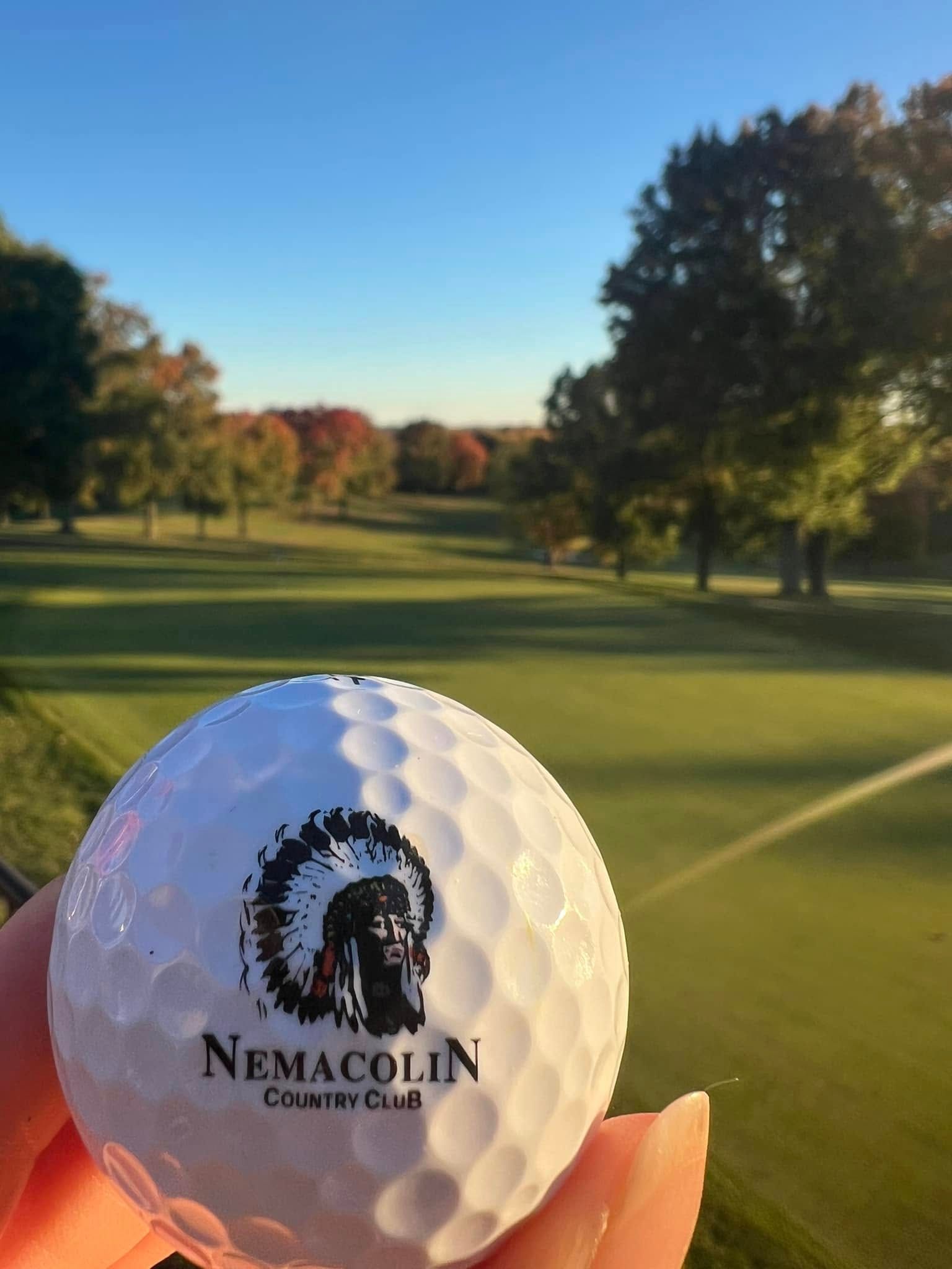 A person is holding a nemacolin golf ball in front of a golf course