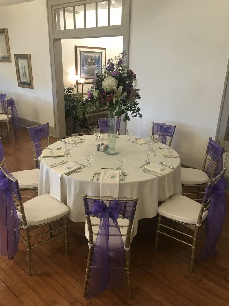 A round table with purple chairs and a vase of flowers on it.