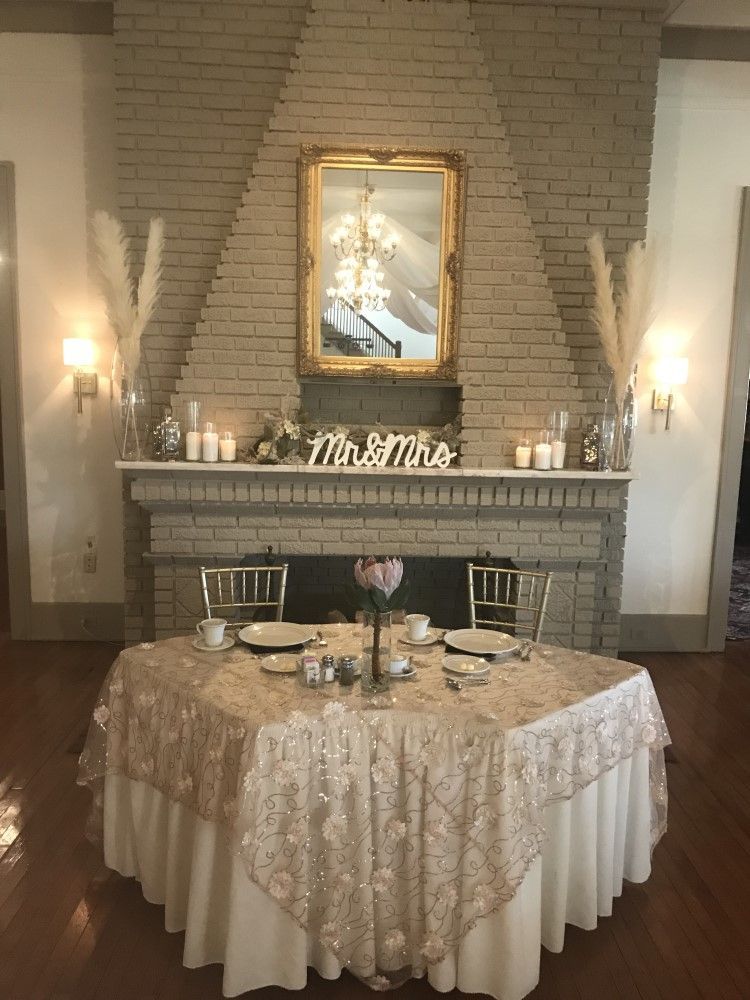 A table set for a wedding reception in front of a fireplace.