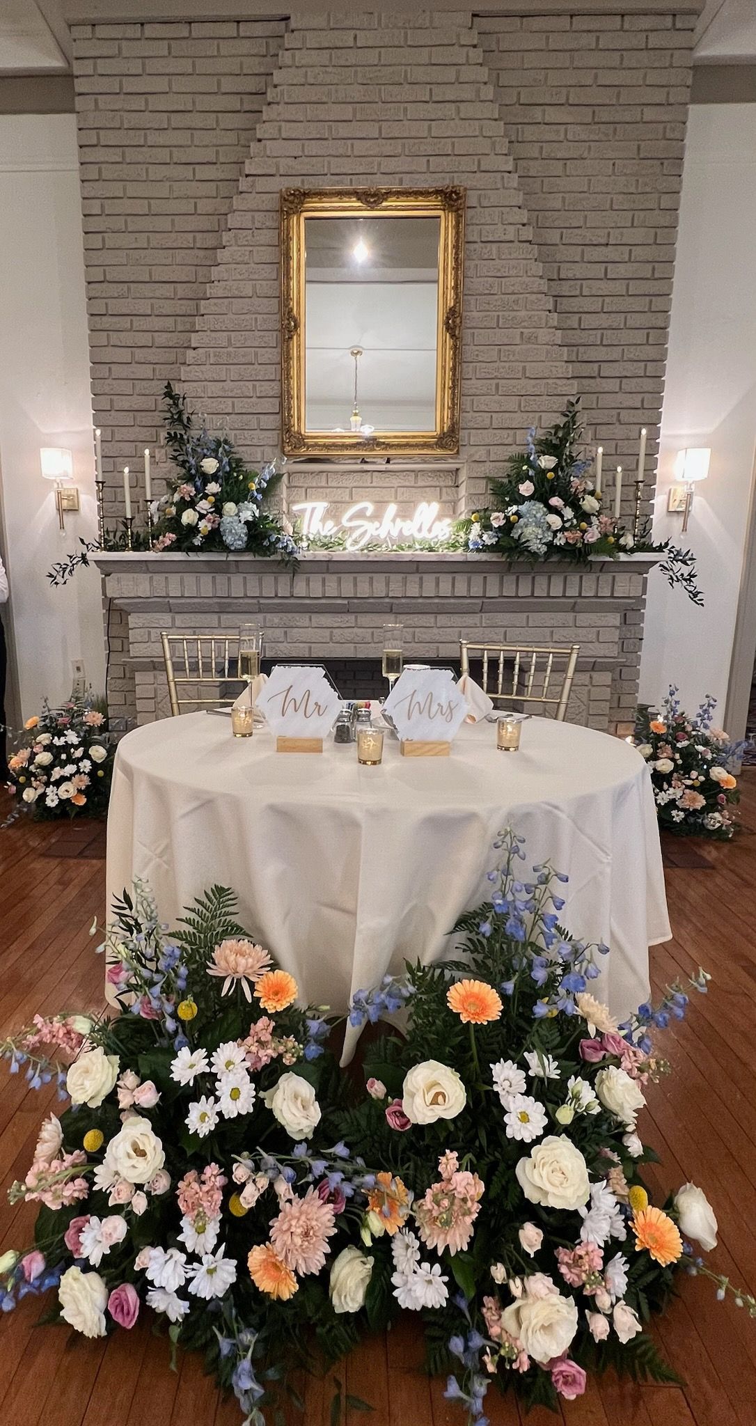There is a table with flowers on it in front of a fireplace.