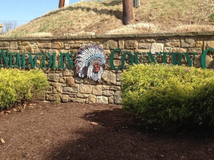 A stone wall with a green sign that says miracle grove