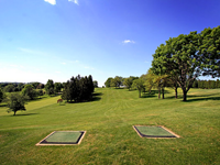 A golf course with two greens and trees on a sunny day.