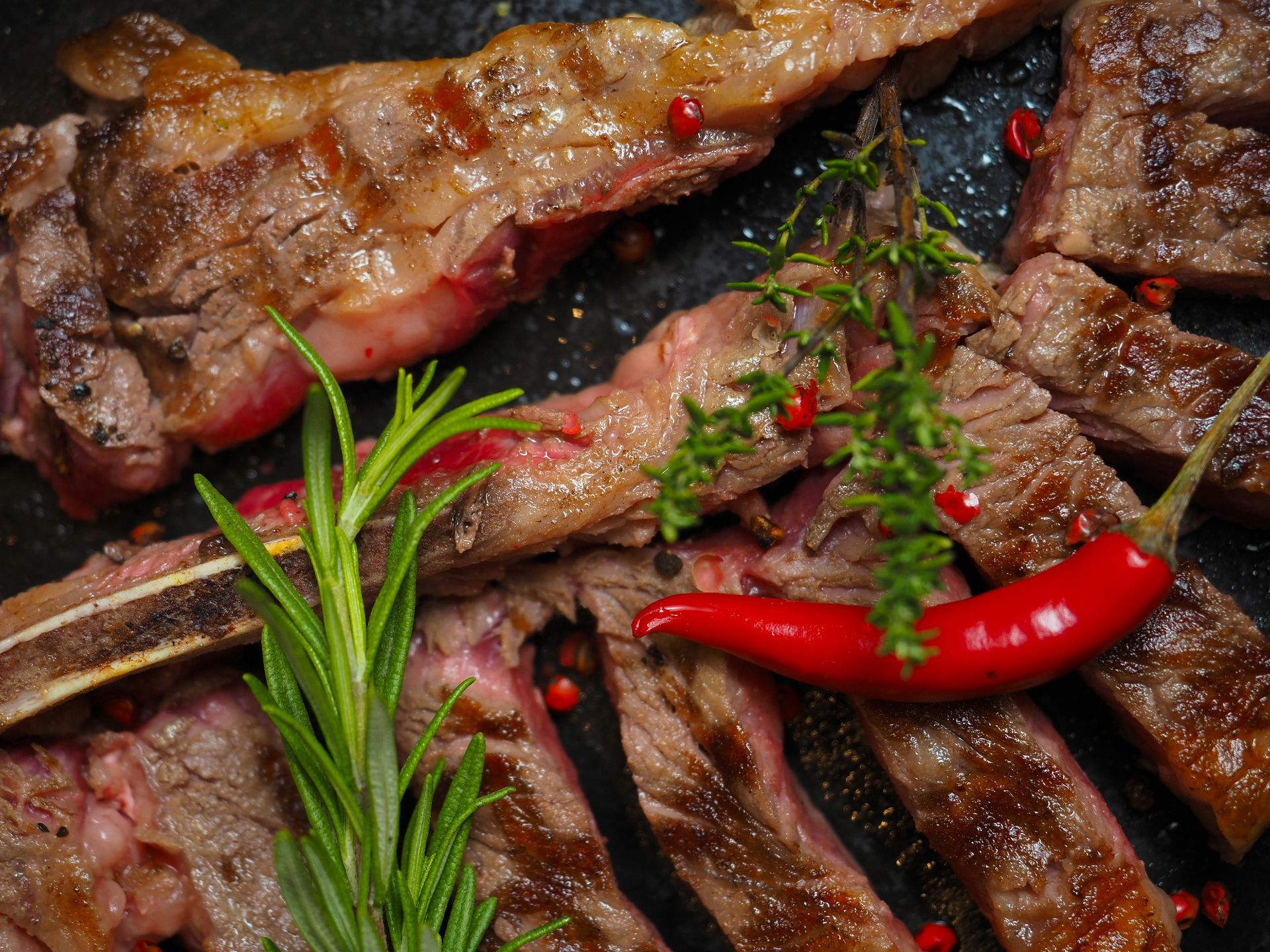 A close up of a steak with a red pepper and rosemary on a pan.
