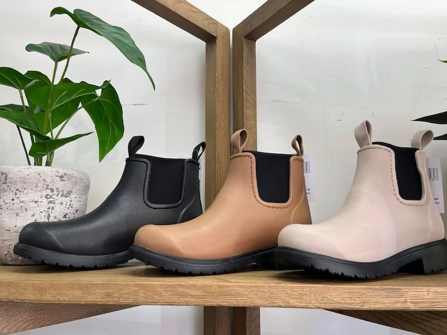Three pairs of rain boots are sitting on a wooden shelf next to a potted — InHouse Homewares in Forster, NSW.