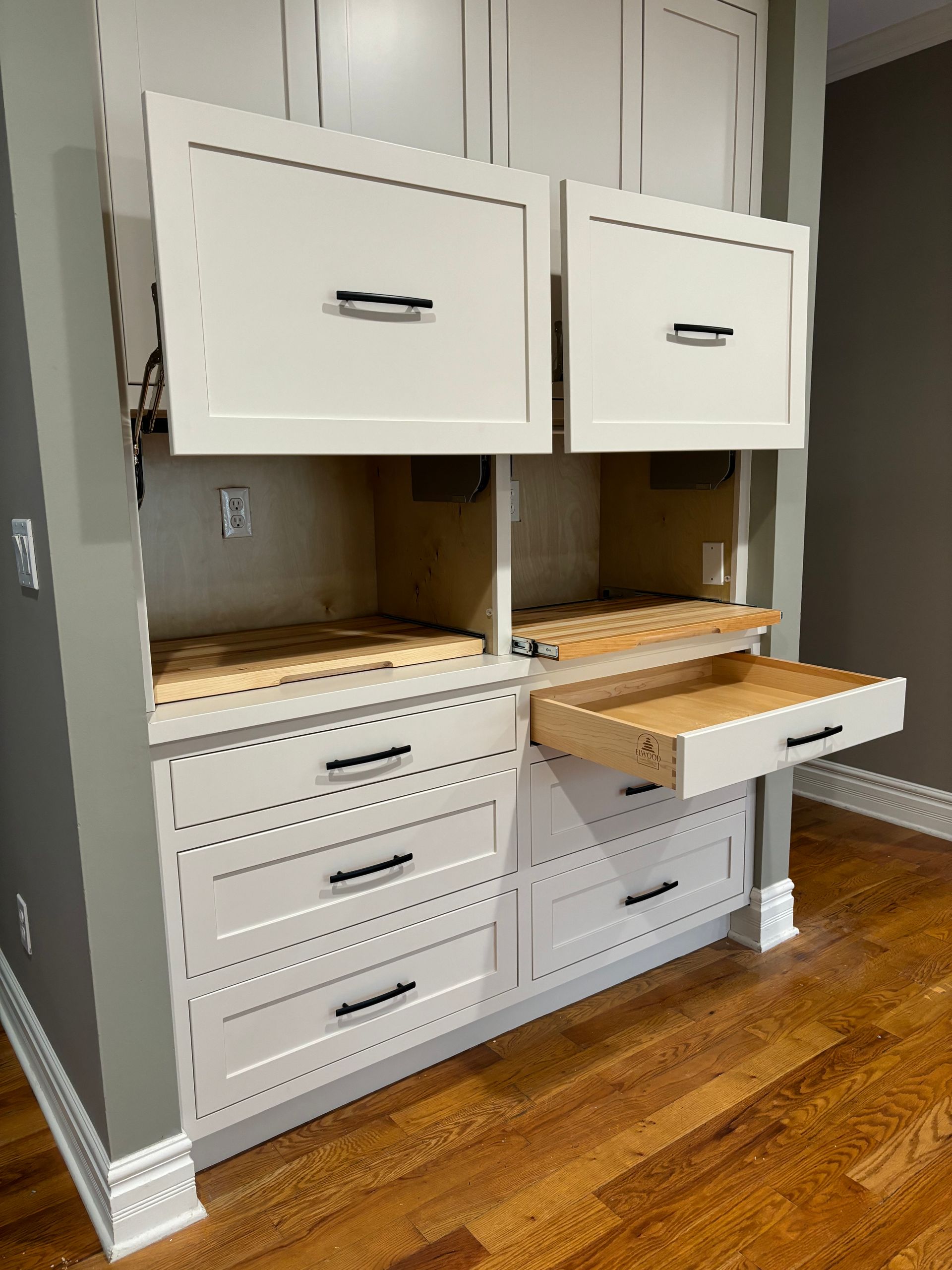 Built-in white cabinets with open doors and drawers. Gray wall, wood floor. Black drawer pulls.