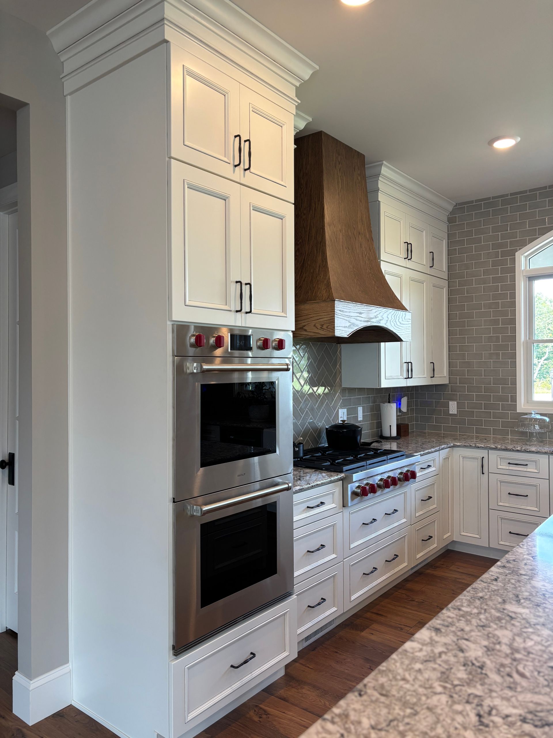 White kitchen with tall cabinets, stainless steel oven, copper range hood, and grey backsplash.