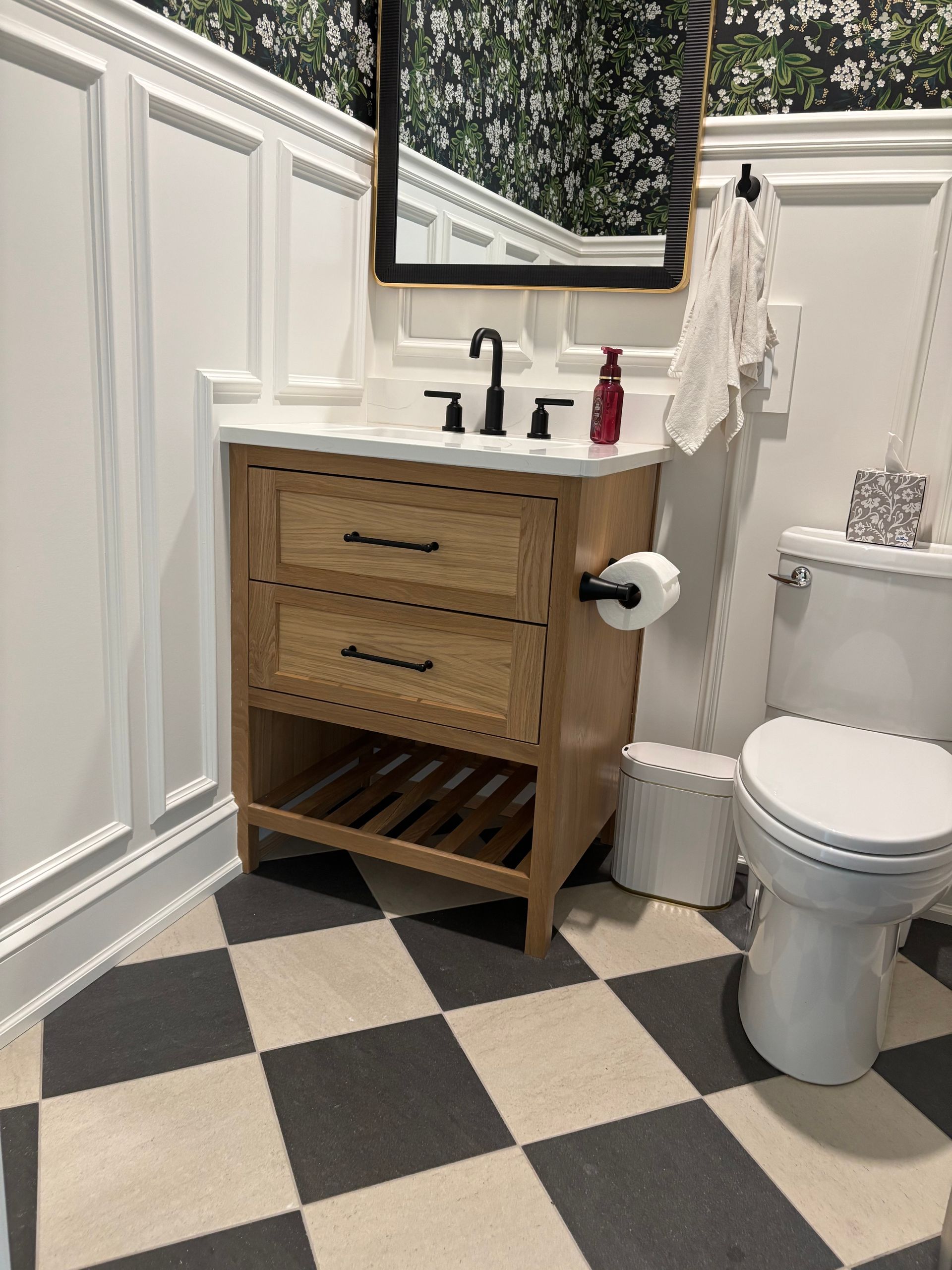 Bathroom with light wood vanity, black fixtures, checkered floor, and floral wallpaper.