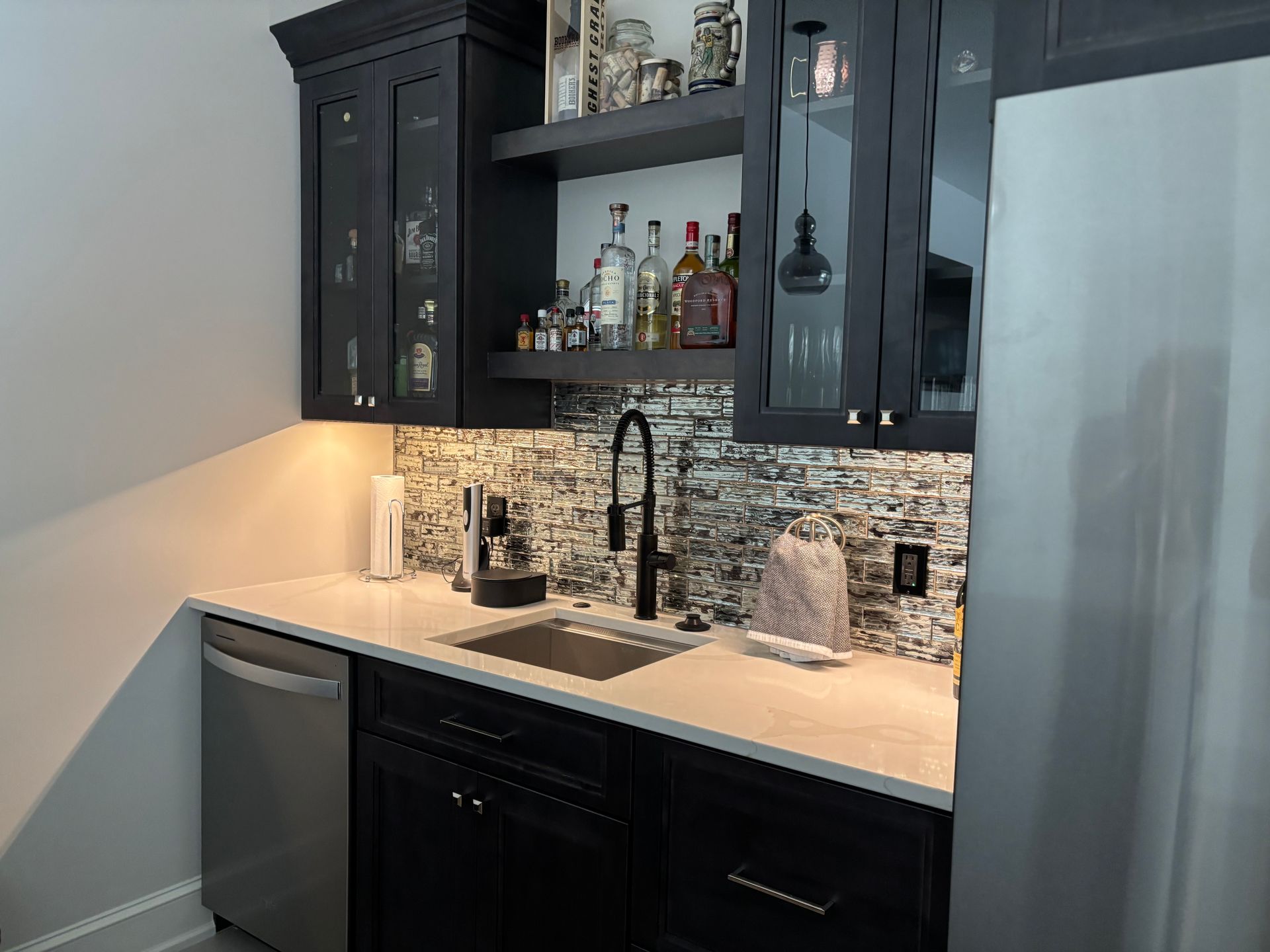 Black home bar with sink, dishwasher, and liquor bottles.