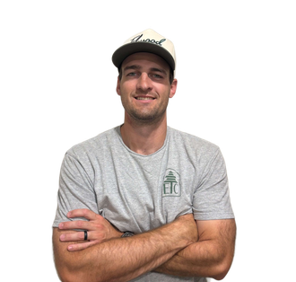 Man wearing cap and gray shirt with arms crossed, smiling at the camera.