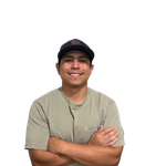 Man wearing a black cap and olive green shirt, arms crossed, smiling at the camera.