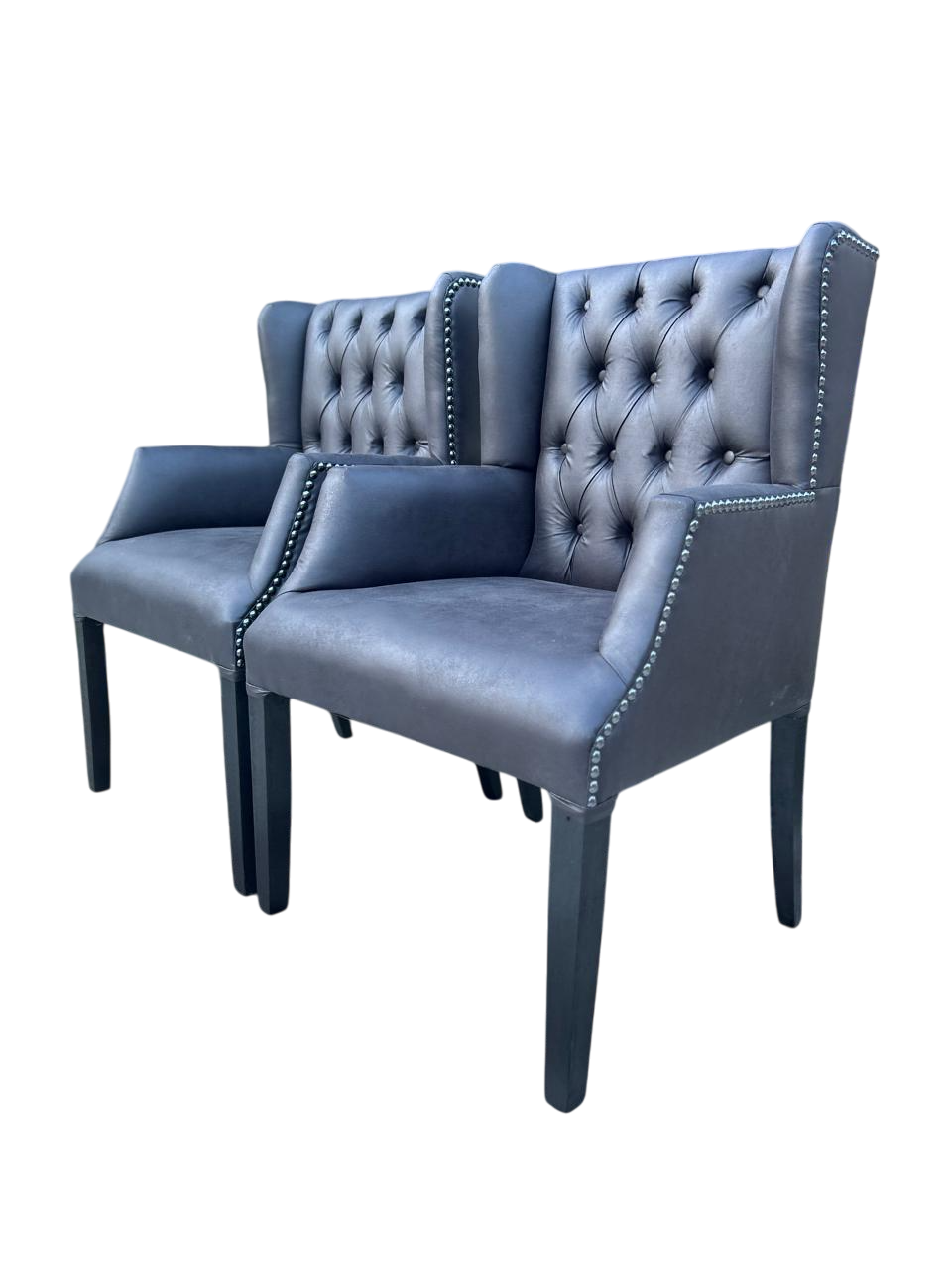 Dos sillones capitoné tapizados en gris con ribete tachonado sobre fondo blanco.