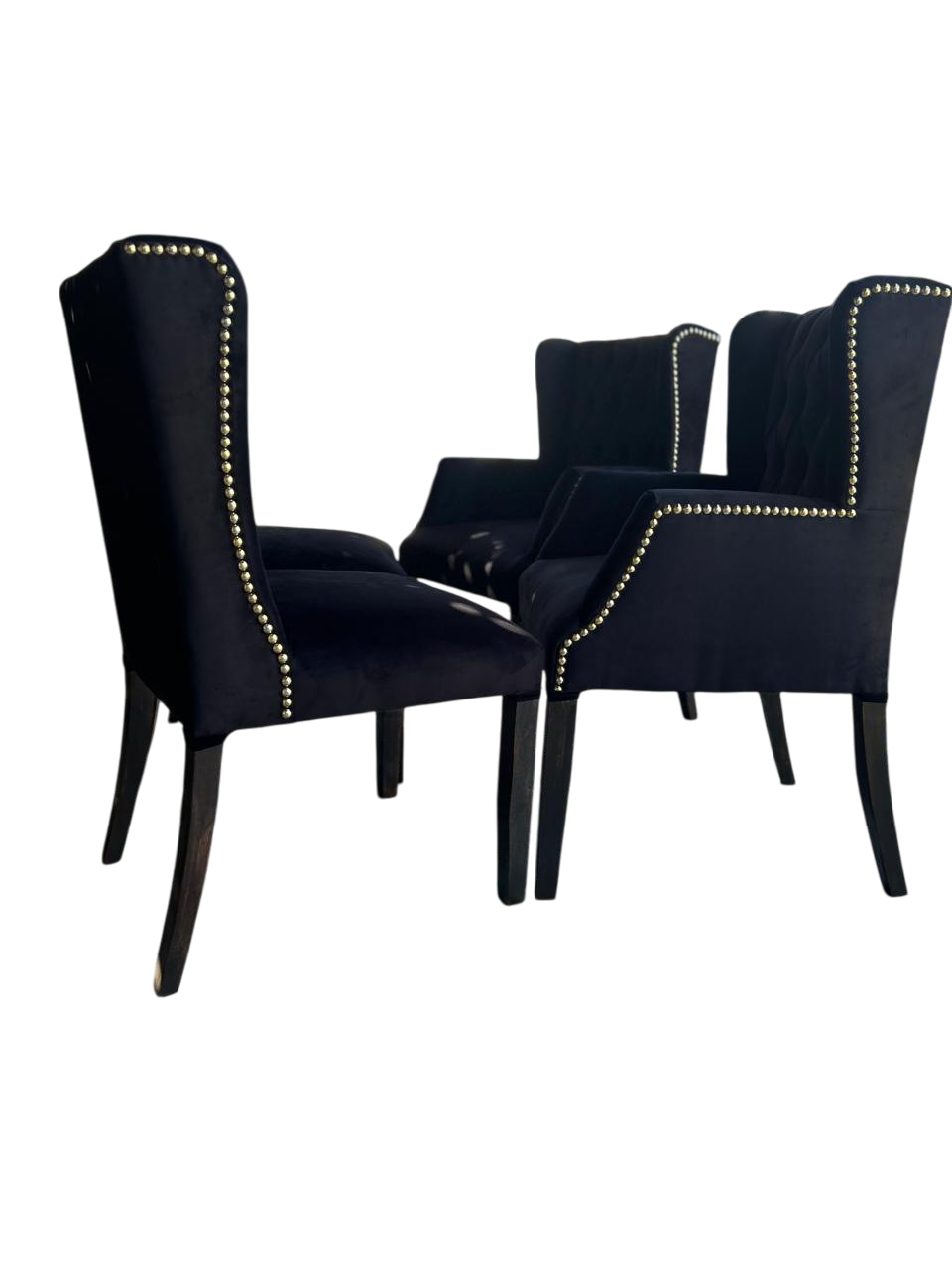 Cuatro sillones negros con tachuelas doradas sobre fondo blanco.