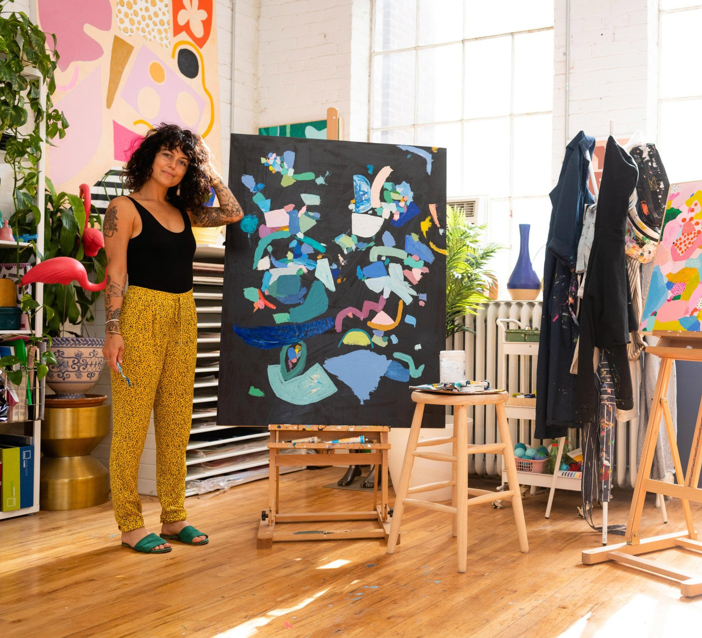 Ashley Mary staged in her studio with a piece of art and aprons spread throughout