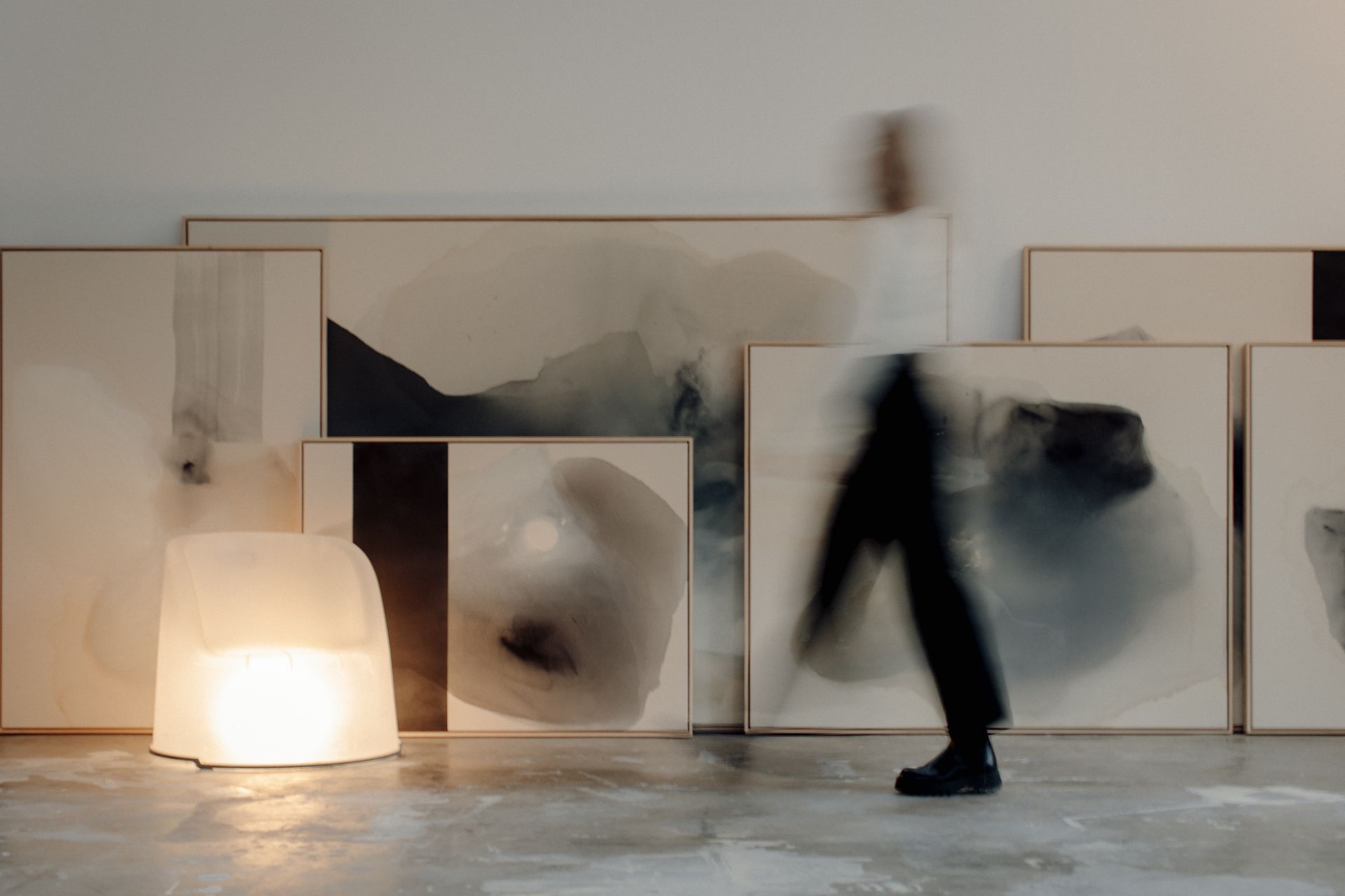 Joy Kinna walking past her large paintings, blurred with movement. in the corner of the shot there is an opaque white chair that has a light inside, giving it the appearance of it glowing.  shot by Brit Gill Photography