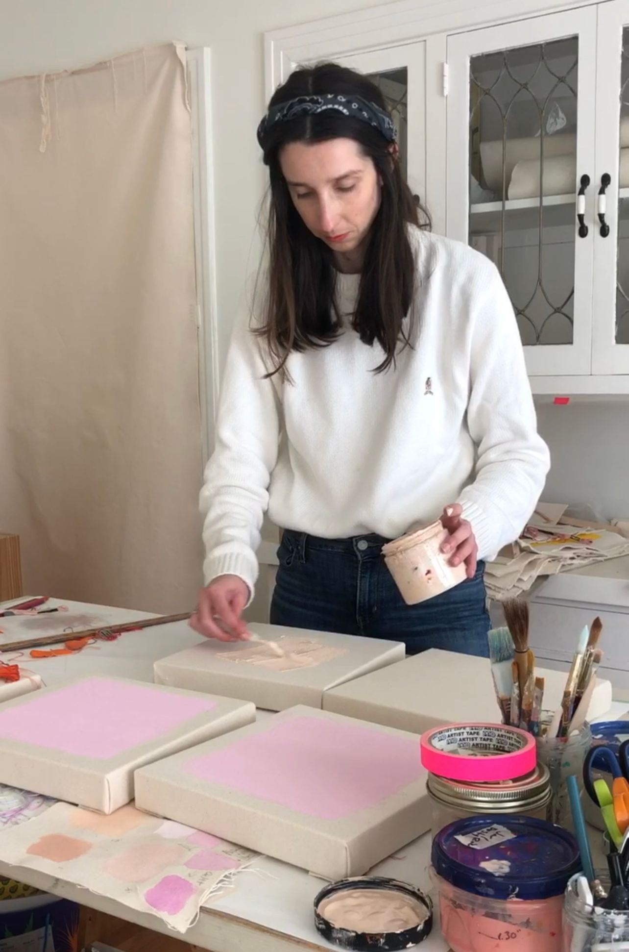 Emily Keating Snyder in her studio painting one of four small canvases in front of her a light shade of pink