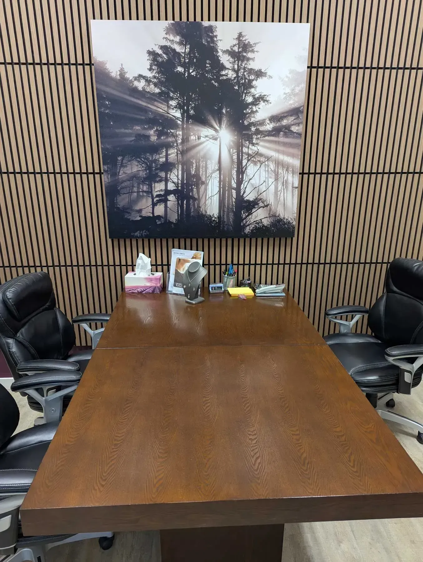 Conference table with two chairs, under a nature scene artwork. Desk has items on it.