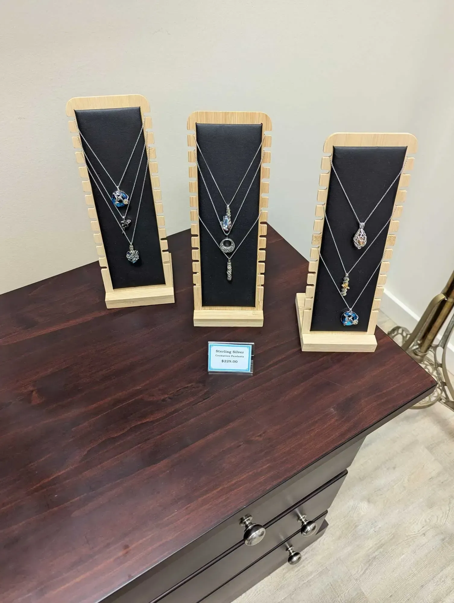 Necklace displays with silver chains and pendants on a dark wood table.