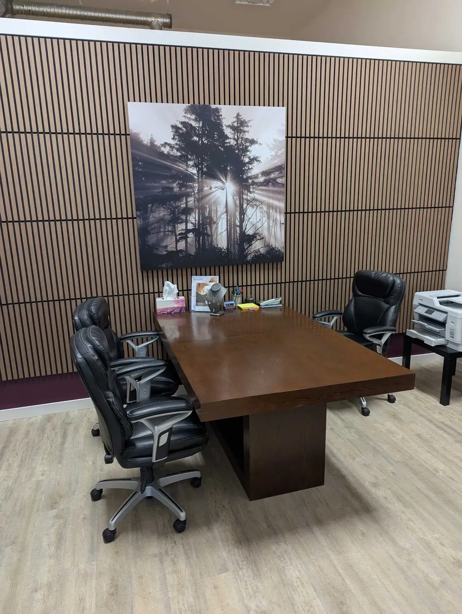 Office with large brown table, leather chairs, art, and patterned wall panels. A printer sits nearby.
