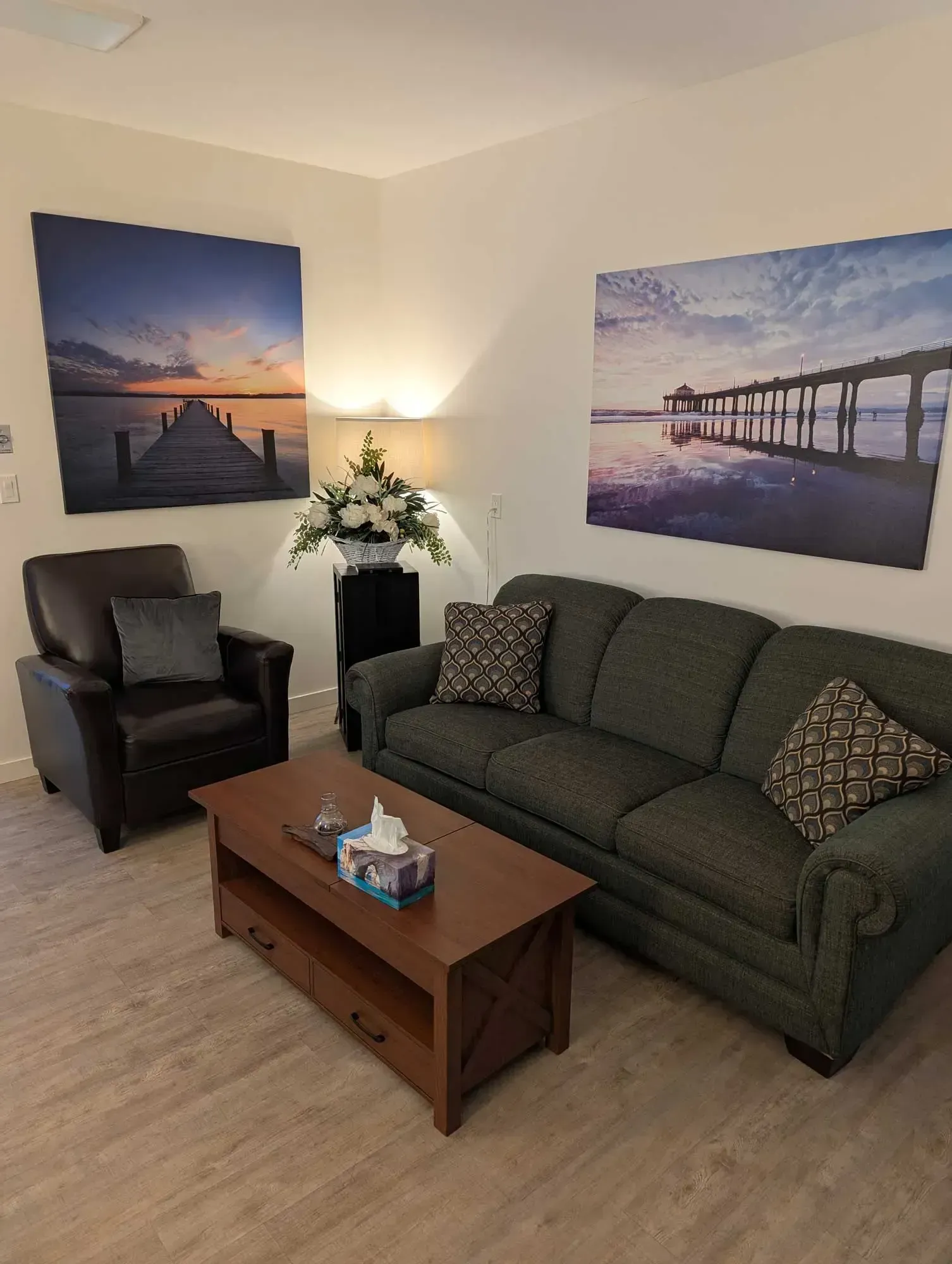 Living room with a dark green couch, leather chair, wooden coffee table, and beach scene art.