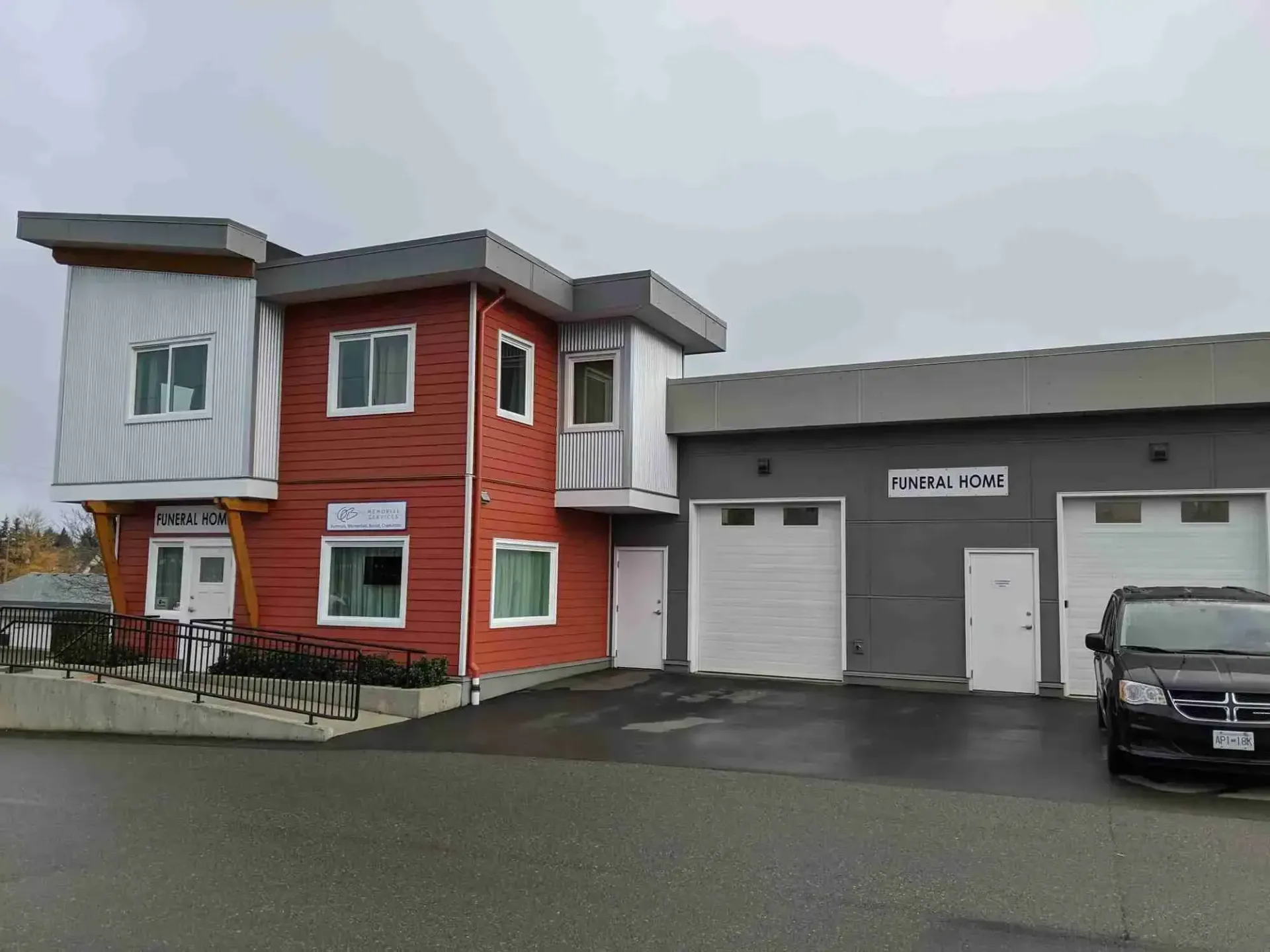 Modern commercial building with two-story red facade, white accents, and garage doors, overcast day.