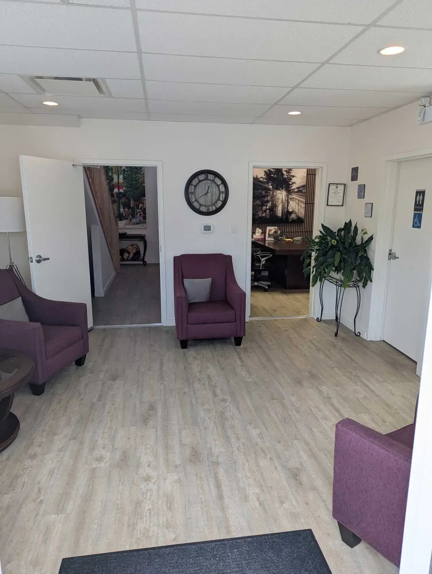 A waiting room with purple armchairs, a large clock, and three doorways.