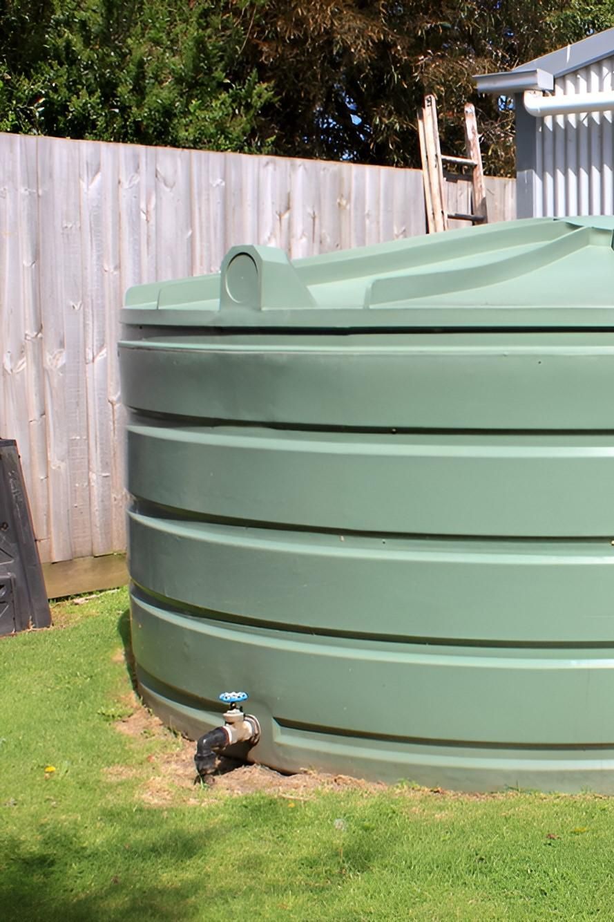 A Green Water Tank is Sitting in the Grass in Front of a Building — Sue's Clear Water in Seaforth, QLD 