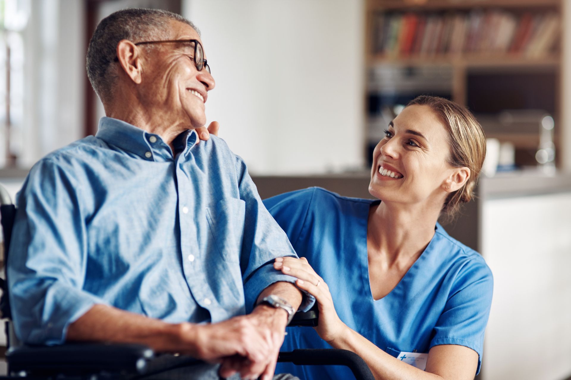 A nurse is holding the hand of an elderly man in a wheelchair.