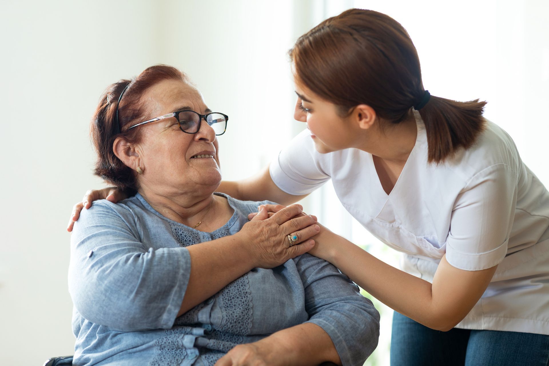 A nurse is comforting an elderly woman in a wheelchair.