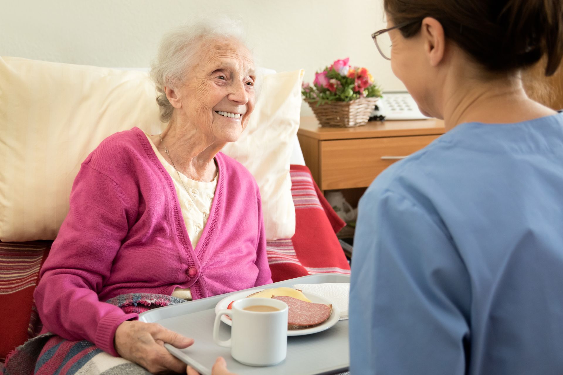A nurse is serving food to an elderly woman in a hospital bed.