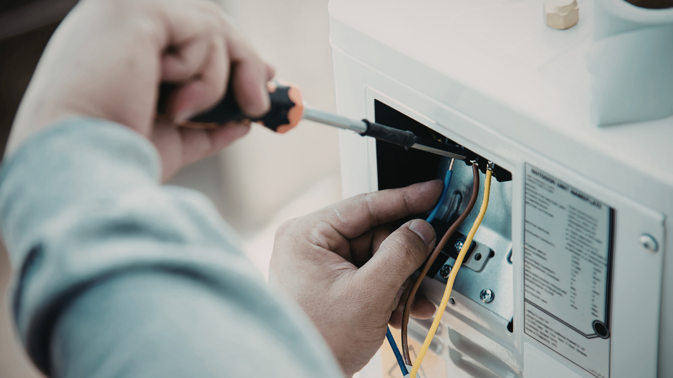 A person uses a screwdriver to connect colored electrical wires inside an appliance control panel.