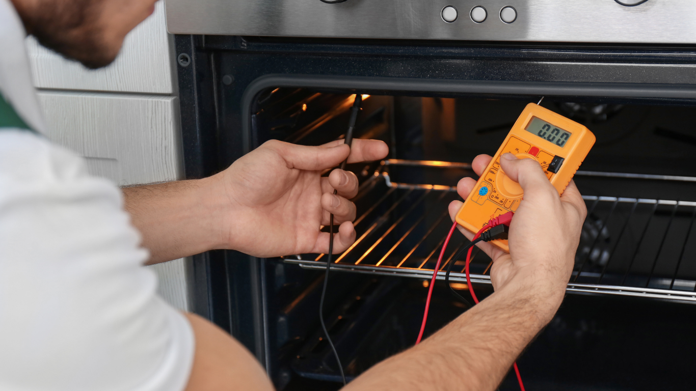 A technician tests an oven's heating element using a yellow digital multimeter.