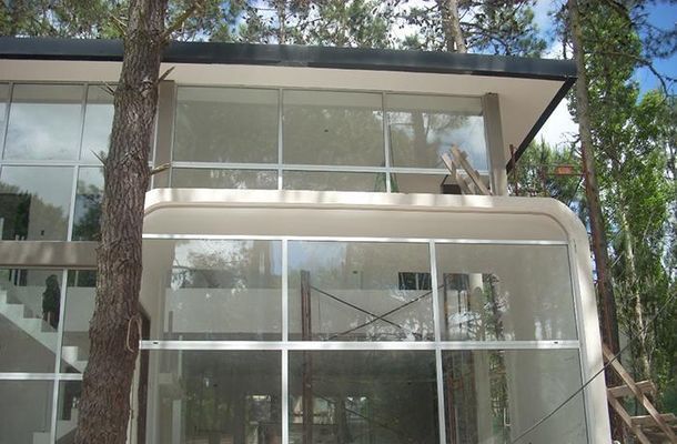 Exterior de una moderna casa de cristal con molduras blancas y árboles en el exterior.